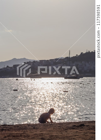 Figure of a little boy on the beach of the sea sparkling at sunset. Beautiful coast with islands, mountains and yachts. Summer holidays concept 117398591