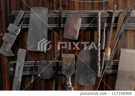 Various woodworking tools hanging neatly on wooden wall, showcasing traditional and modern implements. Tools include chisels, planes, and carving knives 117398906