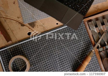 Overhead view showing laptop placed on cutting mats surrounded by crafting tools and materials on work desk depicting active crafting session 117398907