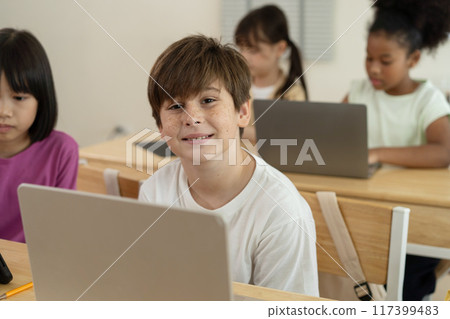 Smiling Caucasian Boy Learning with Laptop in a Diverse and Engaged Elementary Classroom in School 117399483