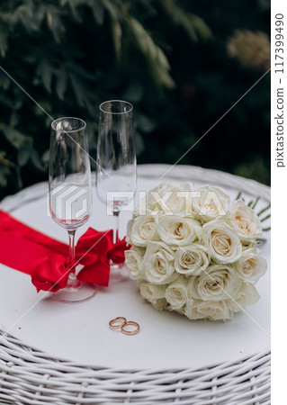 Elegant wedding setting with white roses, wedding rings, and champagne glasses, perfect for celebration Elegant wedding setting with white roses, wedding rings, and champagne glasses, perfect for celebration 117399490