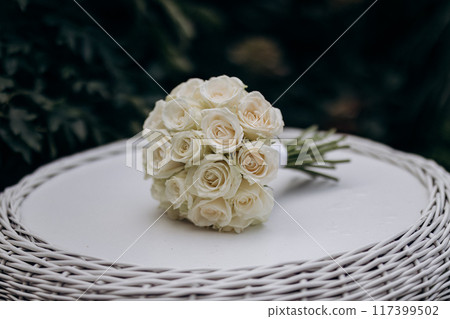 Elegant white rose wedding bouquet on a wicker table, perfect for a romantic ceremony setting 117399502