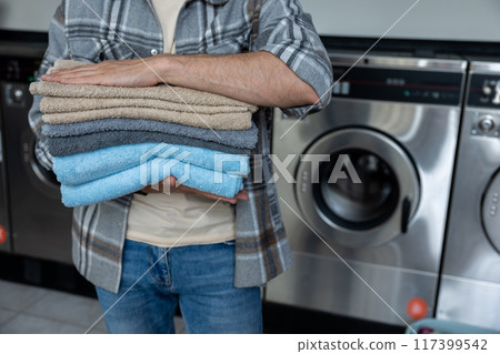 Unrecognizable man carrying stack of towels at public laundromat Unrecognizable man carrying stack of towels at public laundromat 117399542