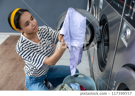 Smiling woman housewife washing clothing at industrial laundromat 117399557