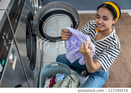 Smiling woman managing household chores at public laundry 117399558