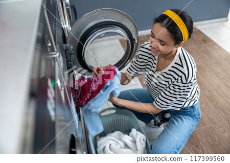 Brunette woman preparing dirty clothes for washing at public laundromat 117399560
