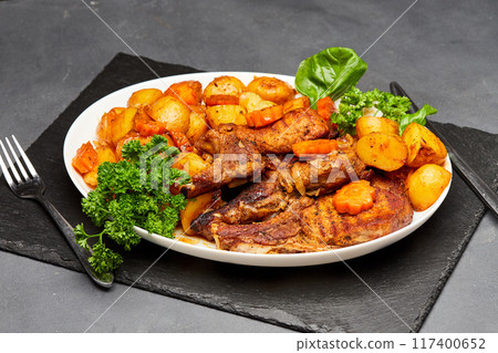 Roasted lamb with golden potatoes and carrots, garnished with fresh herbs for a hearty meal 117400652
