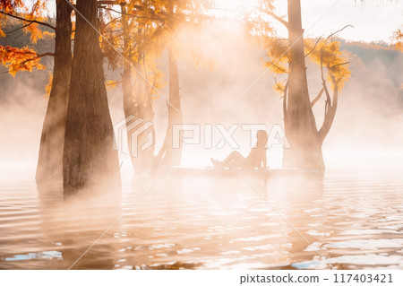 Woman relax on stand up paddle board at lake with morning fog and fall trees 117403421