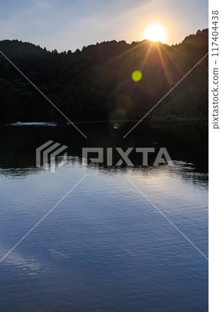 Summer at Nunome Dam in the eastern part of Nara City. Evening view towards the dam lake. The surface of the dam lake illuminated by the setting sun on the opposite bank. 117404438