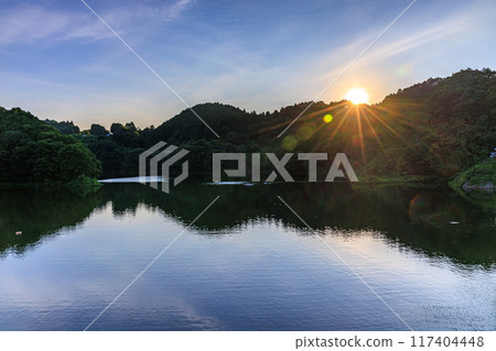 Summer at Nunome Dam in the eastern part of Nara City. Evening view towards the dam lake. The surface of the dam lake illuminated by the setting sun on the opposite bank. 117404448
