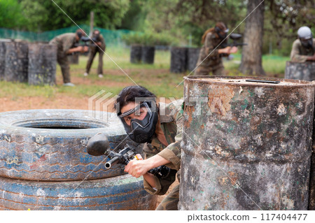 Female paintball player aiming and shooting with gun at opposing team 117404477