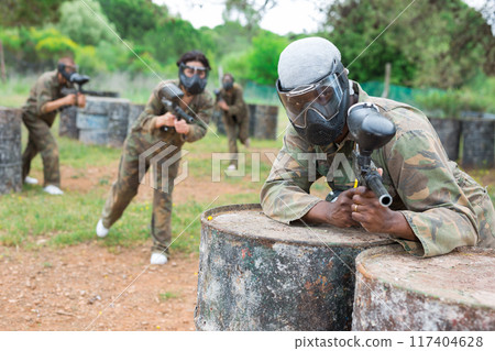 African american man paintball player aiming and shooting with gun at opposing team 117404628
