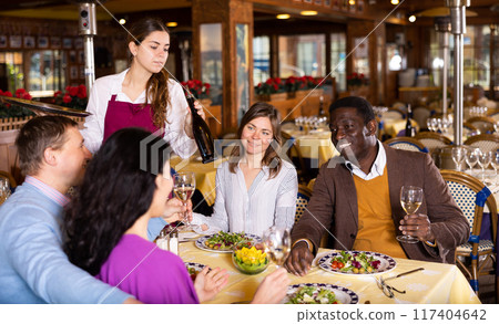 Young waitress serving cheerful people during dinner in restaurant Young waitress serving cheerful people during dinner in restaurant 117404642