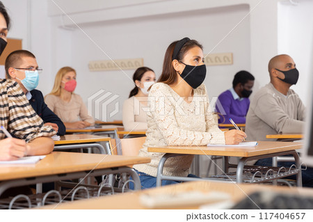Group of students in protective mask listening attentively to teacher explaining material in the classroom 117404657