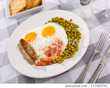 Hearty homemade breakfast - fried eggs with bacon, toasted sausages and large portion of green peas 117404742