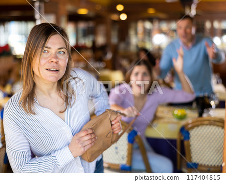 Woman thieves pulls a handbag from a woman during dinner in restaurant 117404815