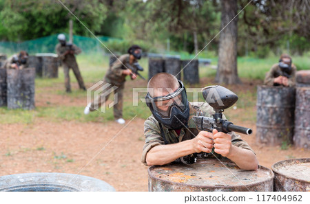 Portrait of man with gun in camouflage on paintball field Portrait of man with gun in camouflage on paintball field 117404962