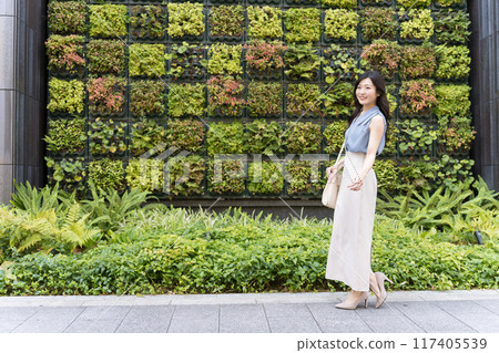 一位女商人在綠牆建築前行走 117405539
