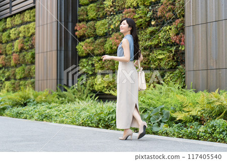 A businesswoman walking in front of a building with green walls 117405540