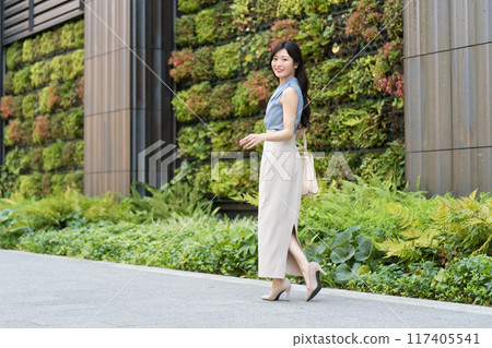 A businesswoman walking in front of a building with green walls 117405541