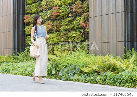 A businesswoman walking in front of a building with green walls 117405543