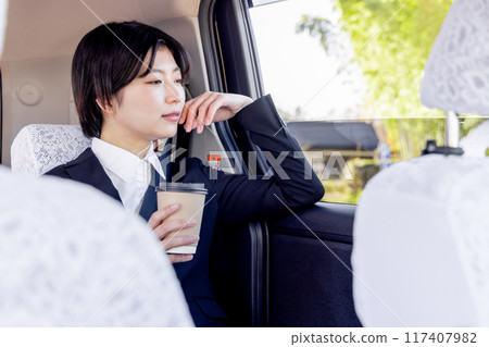 Business woman sitting in the back seat of a taxi and drinking coffee 117407982