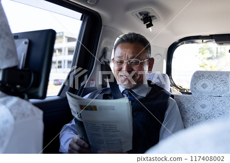 A middle-aged businessman reading an English newspaper in the back seat of a taxi A middle-aged businessman reading an English newspaper in the back seat of a taxi 117408002