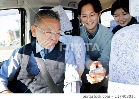 A couple shows their smartphone and tells them their destination in a taxi while traveling 117408033