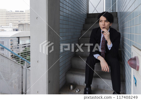 Businessman smoking an electronic cigarette on the emergency stairs 117408249