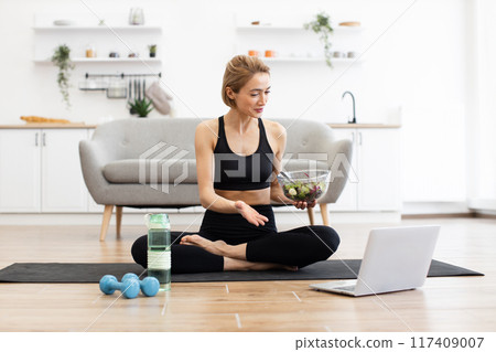 Woman practicing yoga at home with healthy salad and laptop Woman practicing yoga at home with healthy salad and laptop 117409007