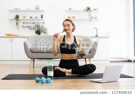 Woman practicing yoga and eating healthy salad at home Woman practicing yoga and eating healthy salad at home 117409010