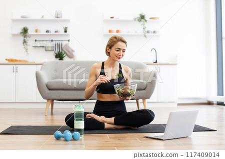 Woman eating salad while watching laptop during workout 117409014
