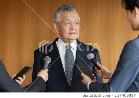 Senior businessman responding to questions from reporters 117409087