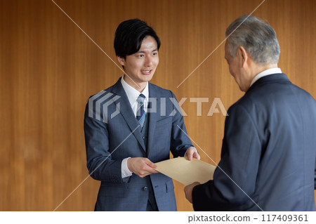 Businessman handing over a confidential envelope Businessman handing over a confidential envelope 117409361