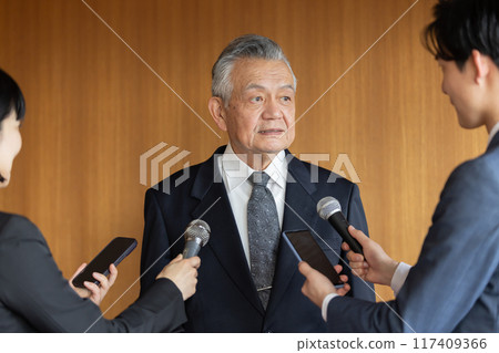 Senior businessman responding to questions from reporters 117409366