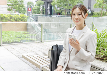 A young woman sitting on a bench and searching on her smartphone A young woman sitting on a bench and searching on her smartphone 117409829