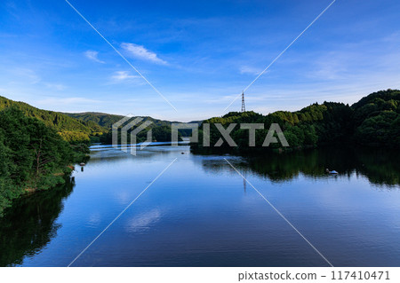 Summer 2024 Evening view of Nunome Dam in eastern Nara City: The water surface of the dam lake spreading out to the southeast and the vast blue sky, the mountain range bathed in the setting sun② 117410471
