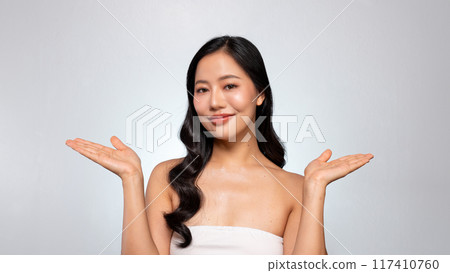 An Asian beauty model poses with her palm open against a grey background, smiling at the camera. 117410760