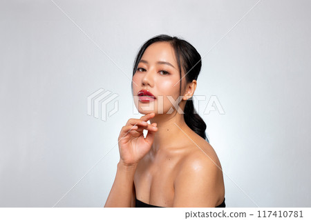 A beautiful Asian woman with perfect makeup and tanned skin poses against a grey studio background. 117410781