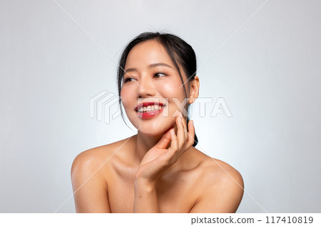 A pretty Asian woman poses against a grey studio background, smiles with her teeth visible. A pretty Asian woman poses against a grey studio background, smiles with her teeth visible. 117410819