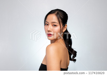 A gorgeous Asian model with healthy tanned skin is posing against a grey studio background. A gorgeous Asian model with healthy tanned skin is posing against a grey studio background. 117410820