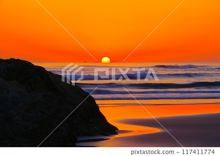 A view of the ocean and beach with the sun rising from a crimson sky in the background Ver1 A view of the ocean and beach with the sun rising from a crimson sky in the background Ver1 117411774