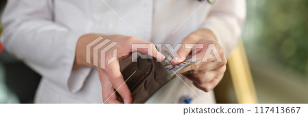 Female doctor putting cash banknotes in wallet Female doctor putting cash banknotes in wallet 117413667