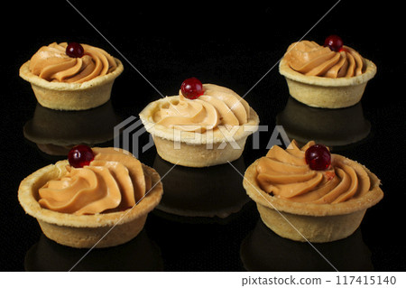 Small cakes with cream on a black background Small cakes with cream on a black background 117415140