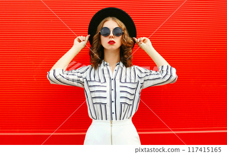 beautiful young woman model wearing white striped shirt, black round hat posing on red background beautiful young woman model wearing white striped shirt, black round hat posing on red background 117415165