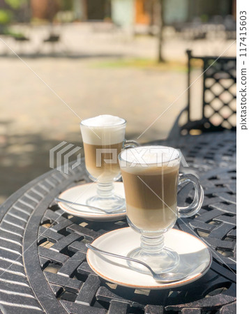 Coffee latte or cappuccino with milk foam in a tall glasses on a wrought iron table in a street 117415603
