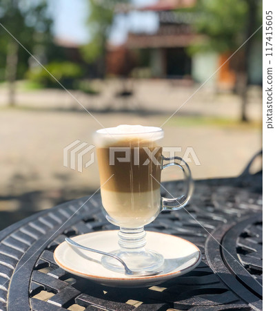 Coffee latte or cappuccino with milk foam in a tall glass on a wrought iron table in a street 117415605