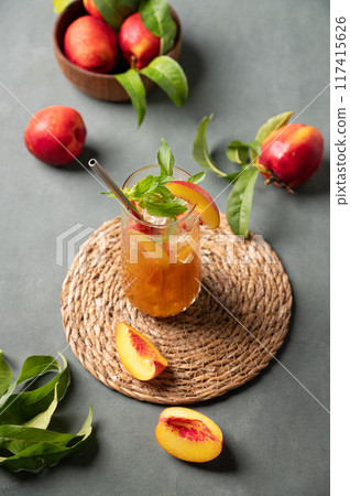 Peach tea with ice and mint on tall glass. Vegan homemade cold summer drink on a dark background Peach tea with ice and mint on tall glass. Vegan homemade cold summer drink on a dark background 117415626