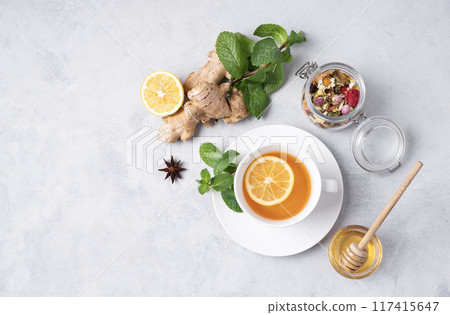 A cup of tea with lemon, honey, mint and ginger on a light background. A cup of tea with lemon, honey, mint and ginger on a light background. 117415647