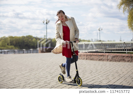 An adult woman is riding a scooter on the street. Active middle-aged woman on a walk. An adult woman is riding a scooter on the street. Active middle-aged woman on a walk. 117415772